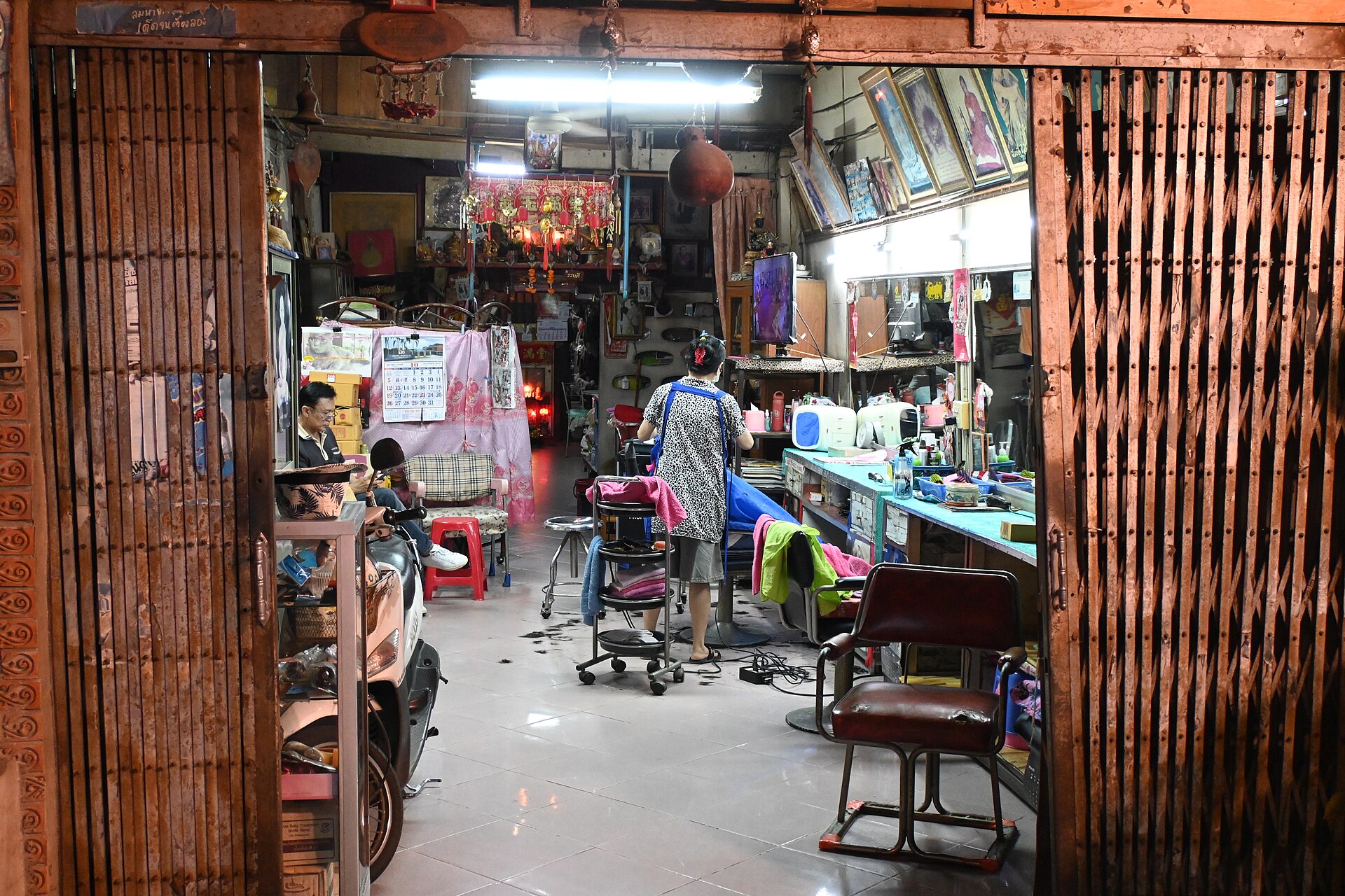 Blick durch ein offenes Scherengitter in einen Friseurladen am Abend